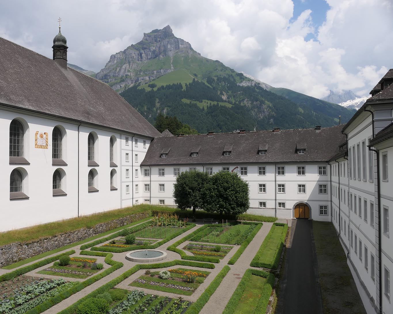 klausurgarten blick nord ost. Spitze Berge und weisse Wolken über dem Klostergarten im Schweizer Engelberg.