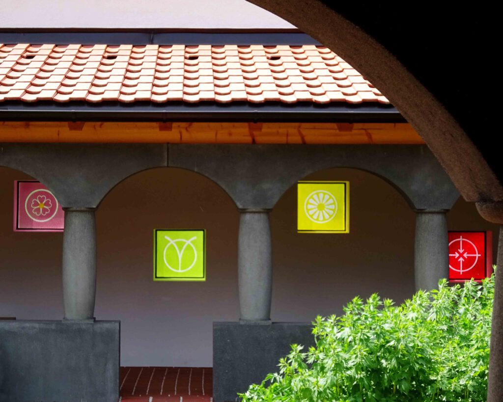 Blumenmandalas sind als farbige Gläser in die glatt verputzten Aussenmauern eingelassen. klostergarten gut aich blumenmantras ms81iuls