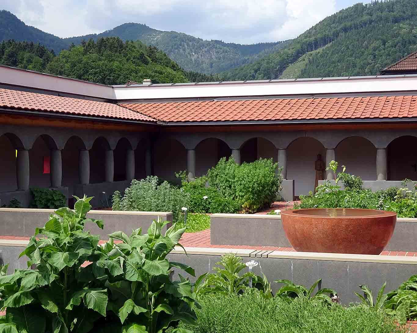 Blick in den Kreuzgang des Klosterguts Aich. Im Mittelpunkt des Kreuzganges mit seinem beeindruckendem Heilkräutergarten sprudelt das Wasser im Brunnen mit seiner steinernen Schale.